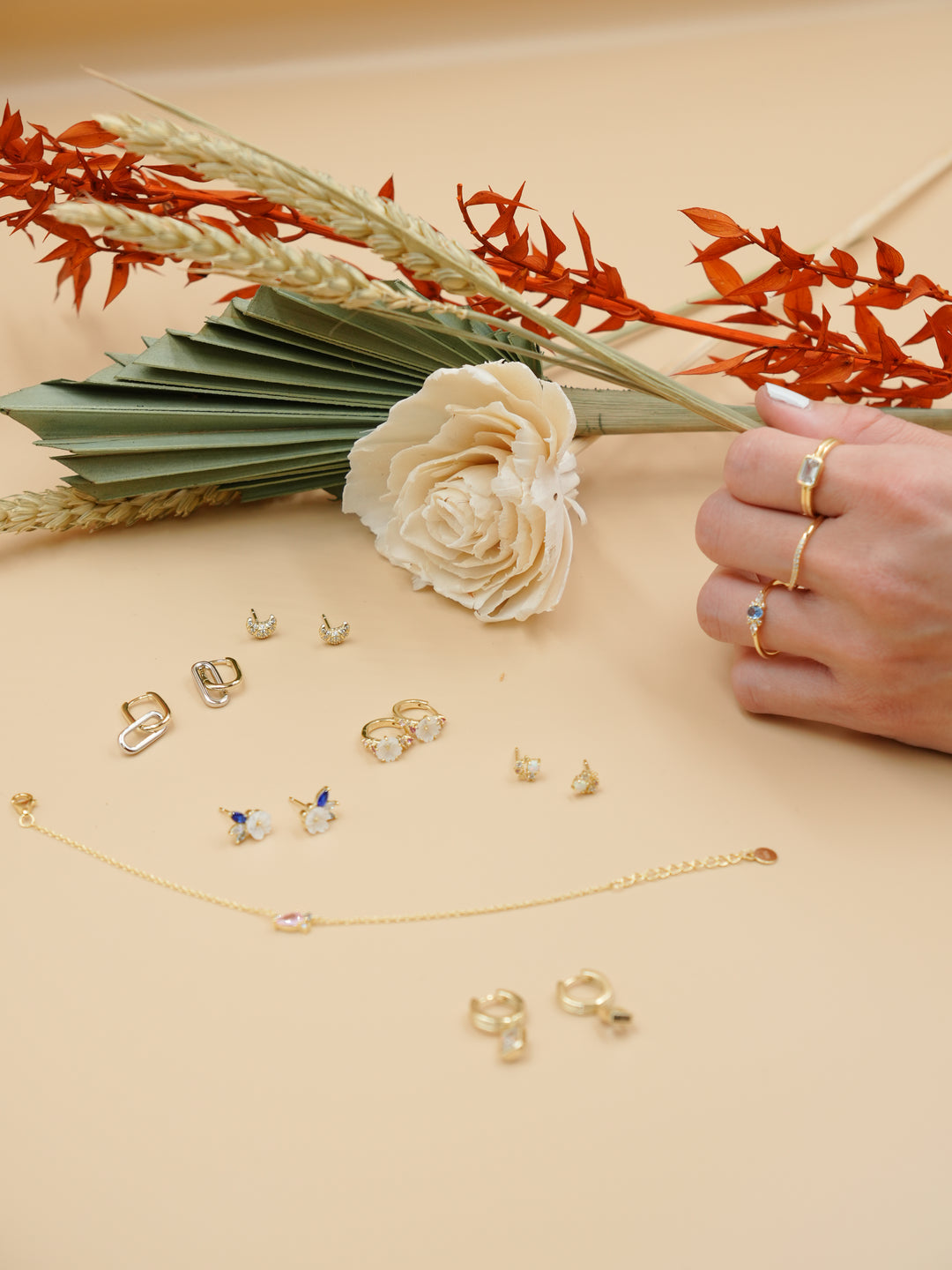 Jewelry including earrings and rings displayed on a beige surface with flowers.