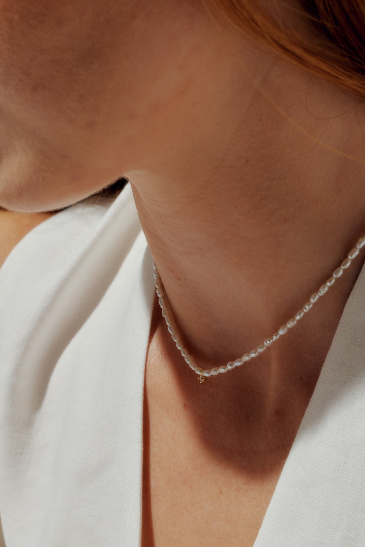 Close-up of a person wearing a delicate silver necklace with a white garment.