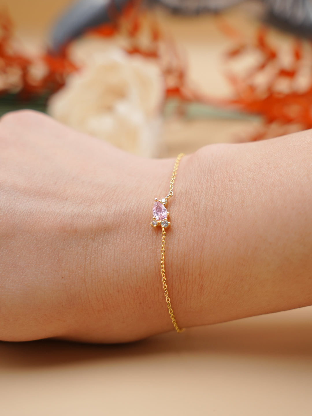 Gold bracelet with a pink gemstone on a wrist against a blurred background
